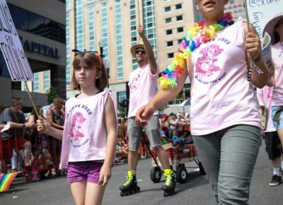 (L–R) Alice, Roller Bladin’ Ben Trentelman and Quincy Koons hold their SLUG signs high as they march in the pride parade. Photo: John Barkiple