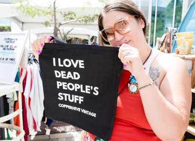 Jaqueline Whitmore showing off the popular “I love dead people’s stuff” tote bag at her shop, Copperhive Vintage. LmSorenson.net