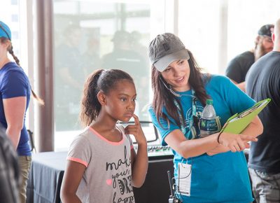 Craft Lake City Artisan and Programs Coordinator Shelbey Lang describes the activities available at the Google Fiber STEM Craft Station including glitter slime and battery-powered cars with recycled milk cap wheels.