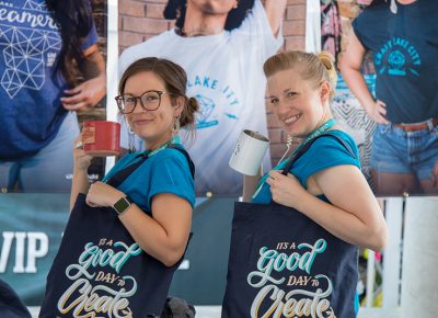 A Craft Lake City Merch Booth Volunteer and Merch Booth Manager Kristin Baird model tote bags and mugs.