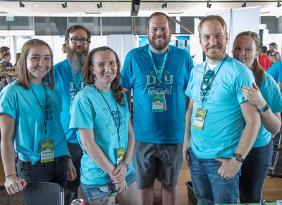 (back row L-R) Craft Lake City STEM Craft Assistants Peter Reed and Chad Dorton stand with four STEM Craft Volunteers. Reed and Dorton managed a rotating crew of volunteers in the Google Fiber STEM building during three days of DIY activities including glitter slime and battery-powered cars with recycled milk cap wheels.