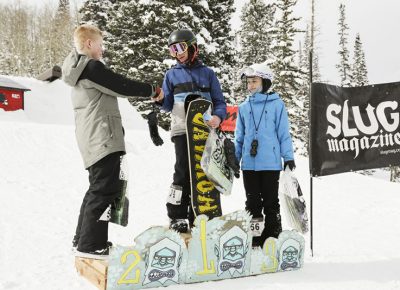 Winners of the mens 17 & under snow show good sportsmanship on the stand. 1st place Isaac Harkness shakes hands with 2nd place Greyson Hawkins, and 3rd place Noah Singer smiles in anticipation for to shake his fellows snowboarders hands.