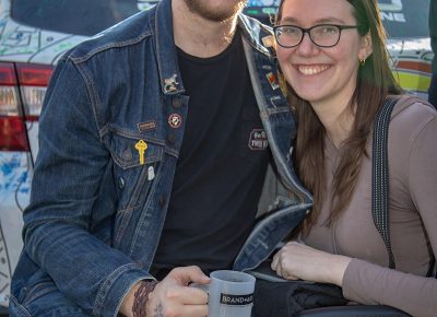 (L-R) Trevor Smith and Chelsea Harmon relax by Mark Miller Subaru’s Art Car. Smith started with a High West Double Rye cocktail called a Spaghetti Western, but now he’s sampling beer. Photo: John Barkiple