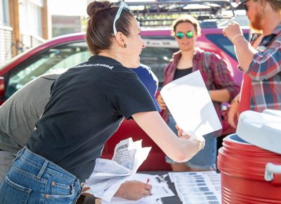 SLUG Magazine’s Angela Brown collects manifests as SLUG Cat racers arrive at SLUG HQ, where racers receive Fat Tire apparel and New Belgium Brewery water bottles. Photo: Kaylynn Gonazlez