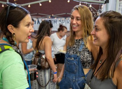 (L-R) In the Makers Building, Angela Brown chats with Mallory Kidwell and Claire Sessler, the owners of In High Spirits Infusions, to discuss possible workshop opportunities after a successful debut at Craft Lake City.