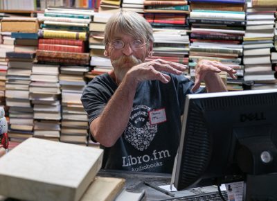 Frank takes in used books for resale and places them on his expanding book glacier in the background—unlike arctic glaciers, it keeps getting bigger and bigger.