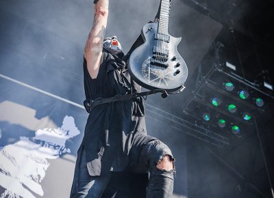 Guitarist of opening band Behemoth rocks with his arms raised to the sky.