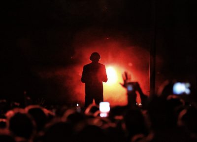 Tyler, the Creator backlit on stage, making music in the dark.