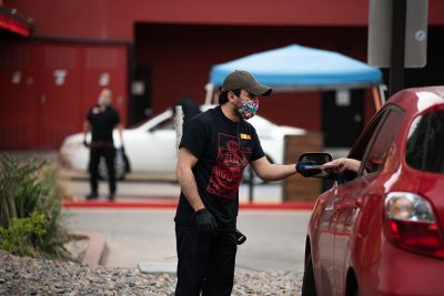 Red Iguana employee Jose “Tony” Arguello carefully handles the tricky maneuver of receiving payment from inside this customer's vehicle. Red Iguana received over 3,000 calls for take-out in the first two days of their curbside model.