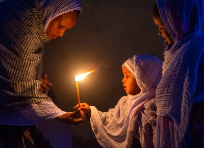 A mother hands a candle to her young daughter, during an early morning candle-light walk in Axum, Ethiopia, on Thursday, March 12, 2020.