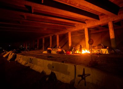 A few of the remaining campers warm themselves by the fire under the freeway over pass, on the last night of Camp Last Hope, on Wednesday, Feb. 3, 2021.