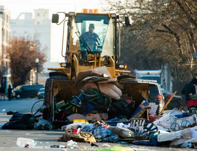 A front-end loader scoops up tents, sleeping bags, blankets and bikes, as the health department sweeps the area, loading everything into dump trucks on Wednesday, Dec. 9, 2020.
