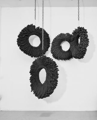 Michael Pribich, Essential, 2020. Installation with 4 wall-mounted and ceiling-suspended elements: brown cotton work gloves over rolled ¼ in. steel rods, steel chain, dimensions vary, each glove wheel 28-32 in. diameter, suspending chain lengths vary. Photo by Max Yawney. Image courtesy of the artist.
