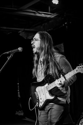 Jared Montgomery of Choice Coin sings passionately while playing on the guitar.