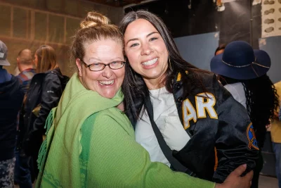 (L–R) Liz Schulte and Annika DiMeo wait in line to buy drinks. DiMeo met Thorpe 20 years ago. She was wearing a vintage “Can’t Drive 55” t-shirt from Sammy Hagar, and he called her out on it. Pretty soon they were singing the lyrics, and just like that, a lifelong friendship took root.