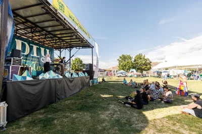 Festival goers sit in the shade while enjoying a live music set from Lane & The Chain.