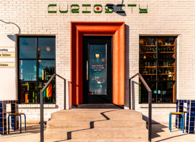 Curiosity's crisp, white, symmetrical building sports a bright pink door frame and its whimsically painted name, create a barrage of inquiries in the minds of pedestrians.