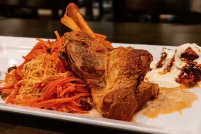 Qabili Palau, Afghanistan's national dish, features a slow-cooked lamb shank served with caramelized carrots and raisins over basmati rice, accompanied by a house salad and savory eggplant doused in garlic-yogurt sauce.