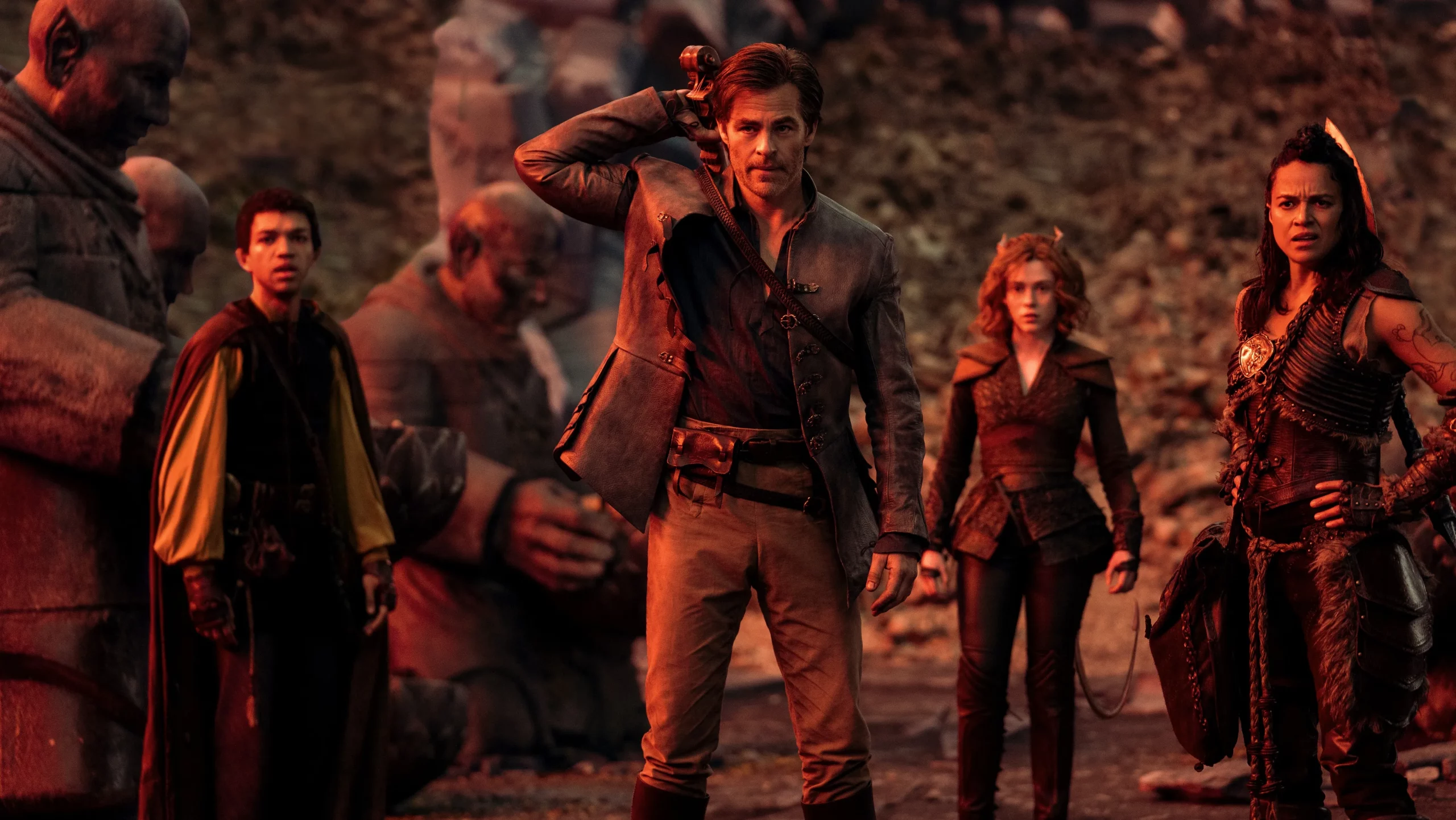 A group of adventurers stands looking toward the camera, altogether taking in a sight. They are bathed in a reddish sunset hue.