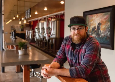 Tim Chappell leans on a partition at Chappell Brewing. His hands are clasped together comfortably. Photo: LmSorenson.net