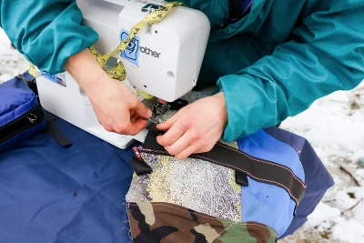 A person uses a sewing machine on a piece of biking equipment outside. Photo: LmSorenson.net