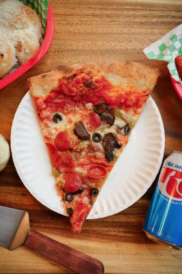 A delicious slice of Snowmobile Pizza's za sits surrounded by beer and bread. Photo: @slc_bites