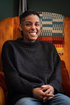 Jade Swayne sits in an orange chair at their home at Iowa House. Photo: Chay Mosqueda