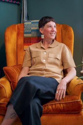 Amanda Madden sits in an orange chair at their home, Iowa House. Photo: Chay Mosqueda