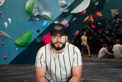 Carlos Vizcarra sits in front of a climbing wall.