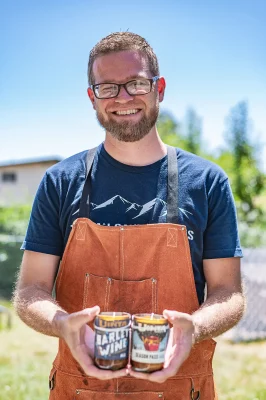 Wearing an orange apron and blue shirt, Tappan shows off two handmade candles. 