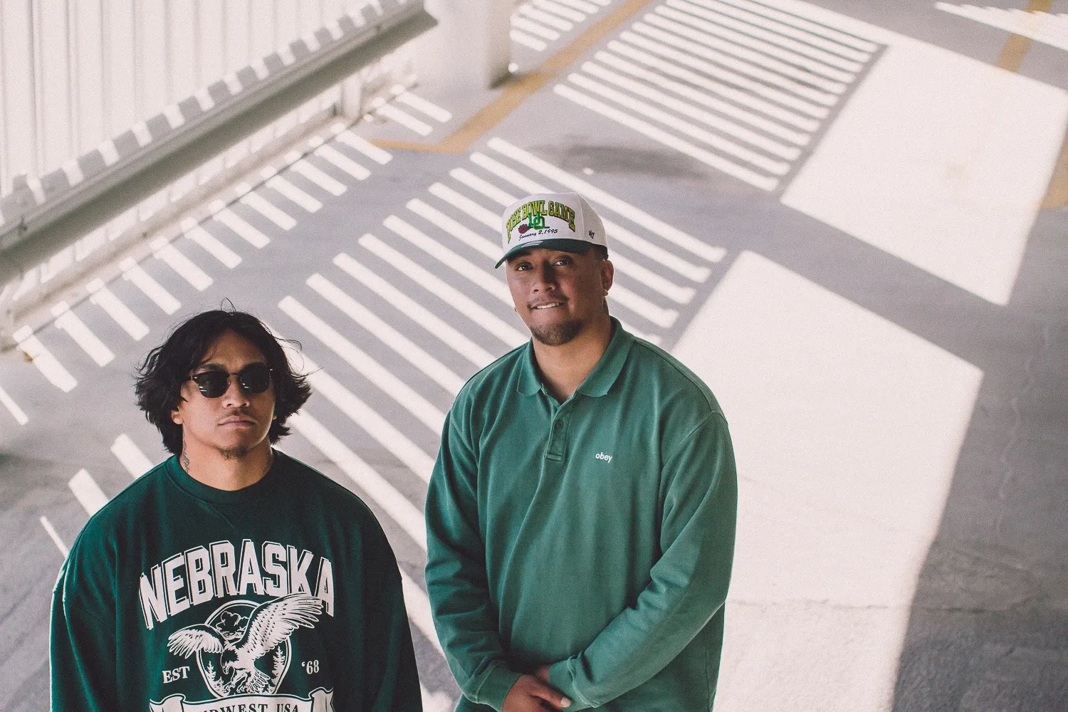 The brother duo of Roses On The Moon stands at the top of a parking garage wearing green sweatshirts.