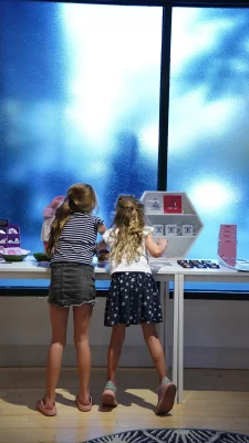 Two young children at a table with art for sale on it.