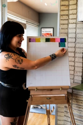 Velasquez poses with a partially completed work on an easel to show the process of her beadwork.