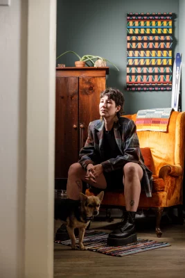 Amanda Madden sits in an orange velvet chair with their dog at their feet.