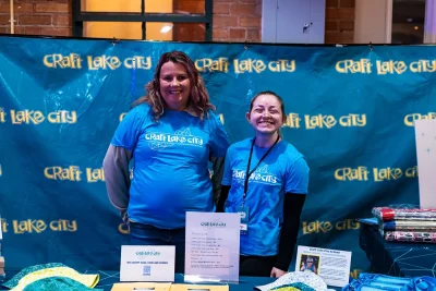 Two Craft Lake City volunteers stand at the event booth in front of a Craft Lake City banner.