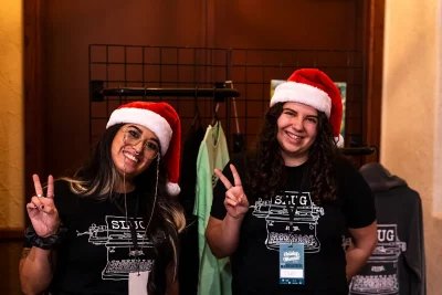 Two SLUG Magazine representatives wear SLUG Merchandise and Santa hats at the SLUG booth.