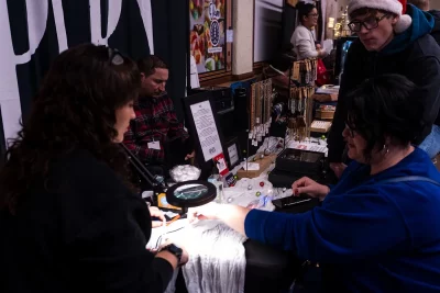 A customer holds their hand underneath a magnifying glass to be fit at SPARX permanent jewelry.