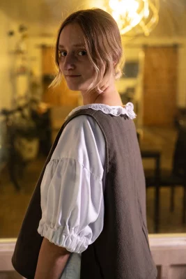 Abigail Rue Jenson looks over her shoulder in front of a window to her home, wearing a blouse with puffy sleeves.