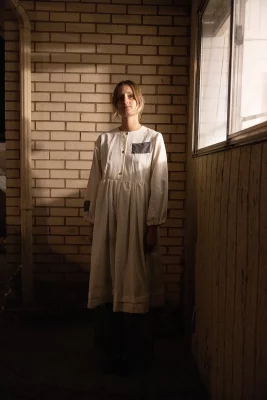 Abigail Rue Jenson stands wearing a dress from her "Patched Up" clothing series against a brick background.