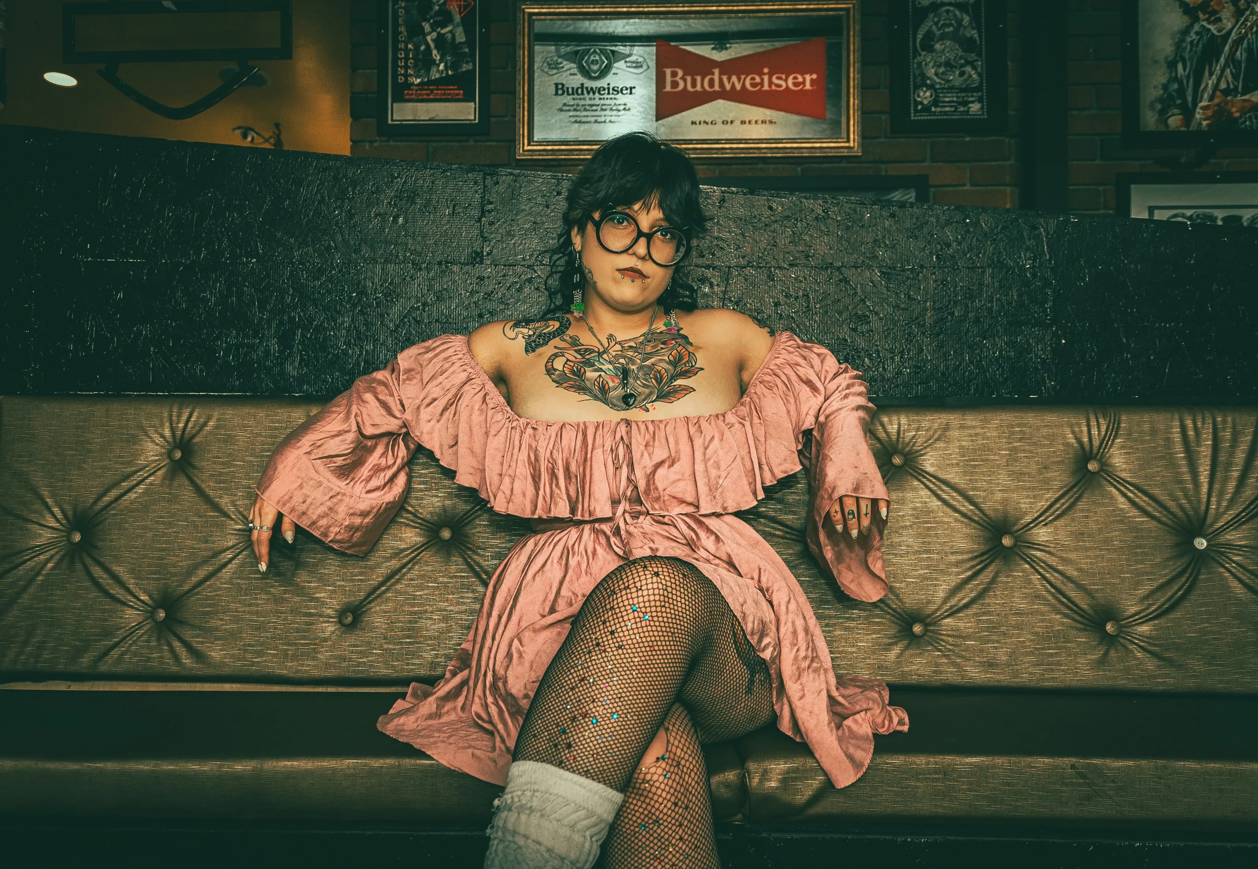 Kat Aleman wears a pink off-the-shoulder dress while leaning against a sofa.