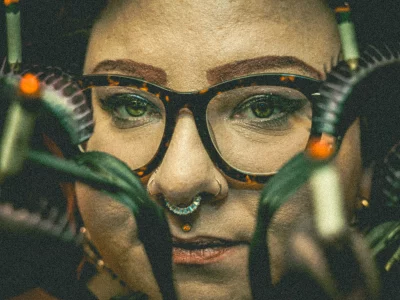 Kaycee Lane looks from behind a sculpture of venus fly traps smoking cigarettes.