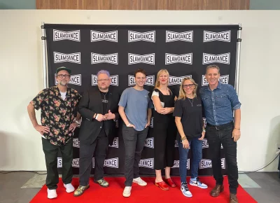 The Slamdance team smiles against a branded back drop.