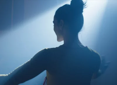 The back of a woman's head with her hair in a bun illuminated by blue light.