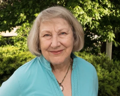 Debora Threedy smiles in front of trees and bushes.