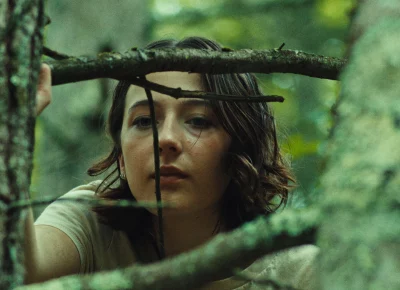 A teenage girl peeks through tree branches.