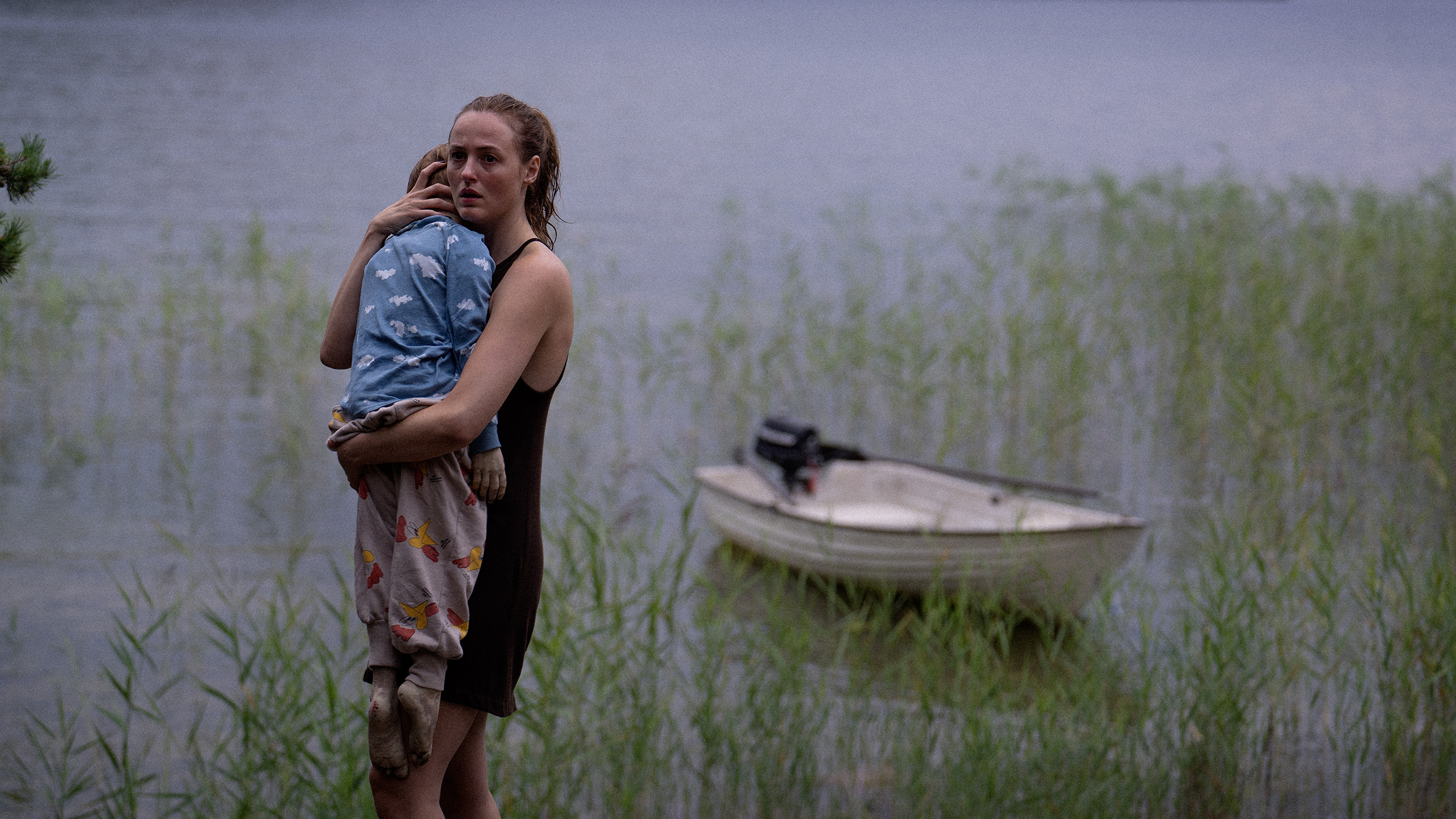 A woman holds her child in front of a lake.
