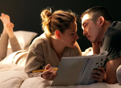 A couple looks into each other's eyes while lying on a bed.