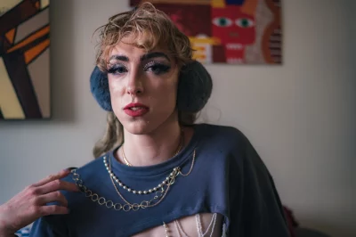 Robin D'Banc wears earmuffs, a crop top and gold chains and pearls.