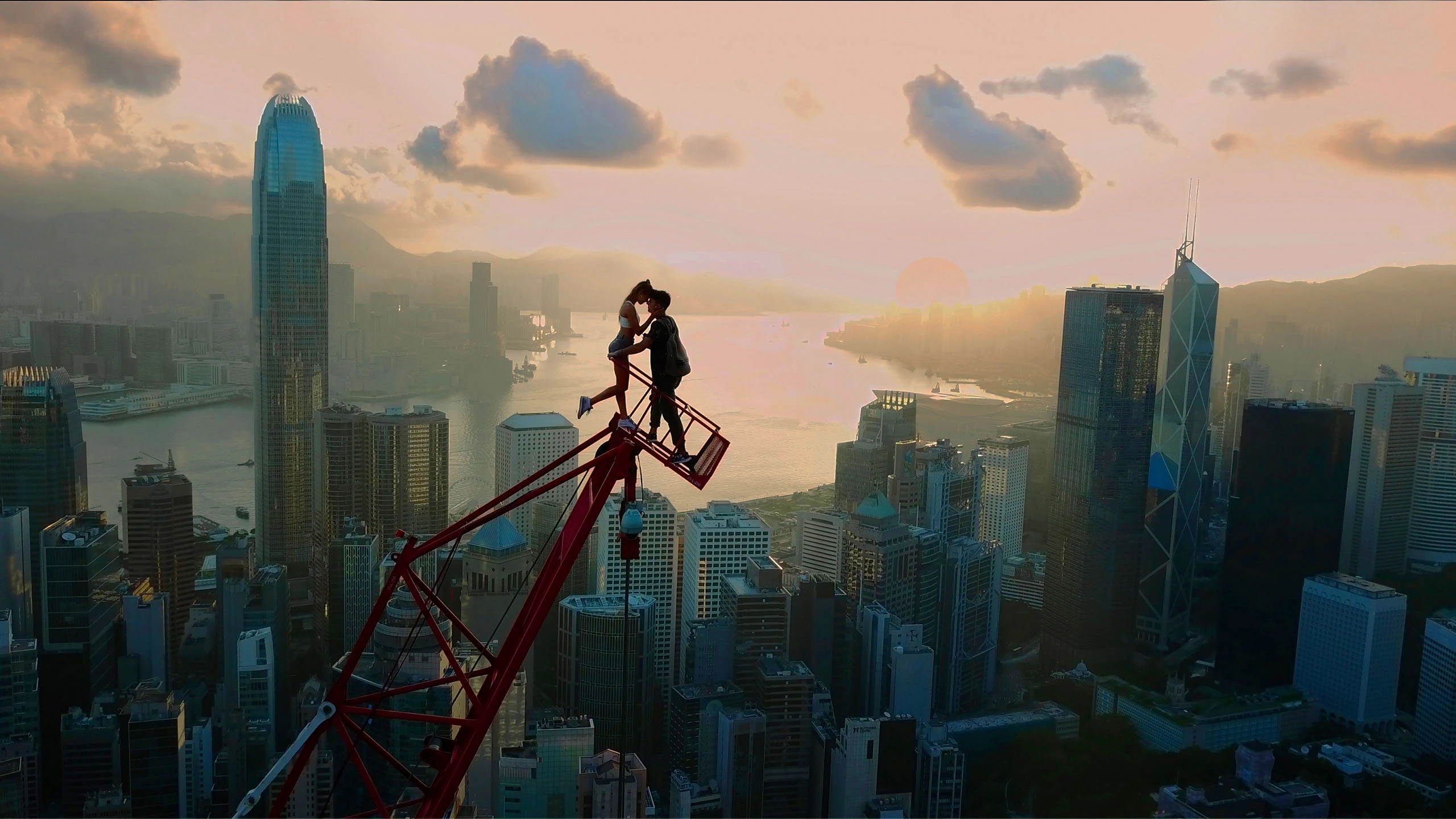 A couple kiss on a crane overlooking a city skyline.