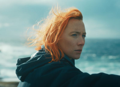 Saorise Ronan's character Rona has bright, orange hair and gazes out across the seaside.
